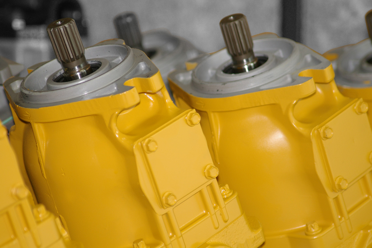 Yellow painted Hydraulex Reman Vickers hydraulic pumps lined up on bench.