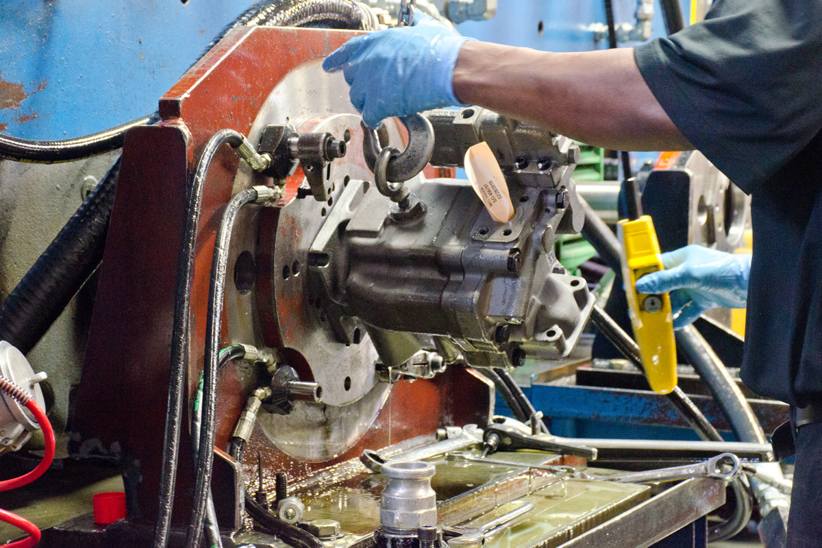 A hydraulic technician testing a hydraulic pump on a hydraulic test stand - with a crane attached to the unit.